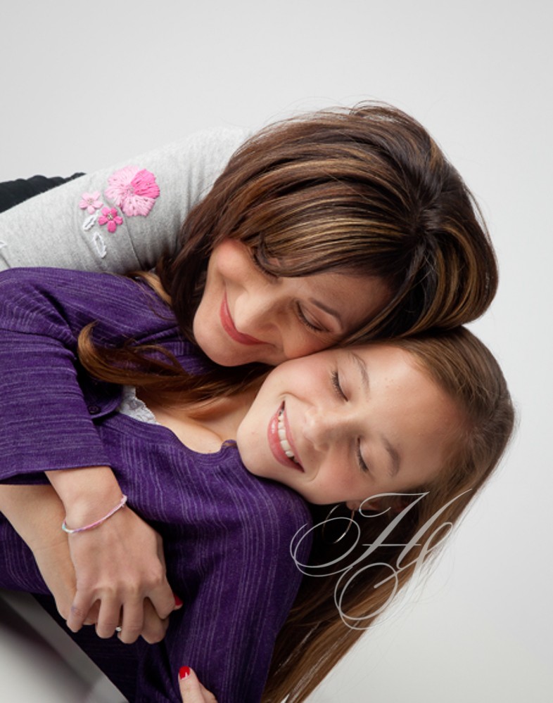 A woman and girl laying on the ground hugging.
