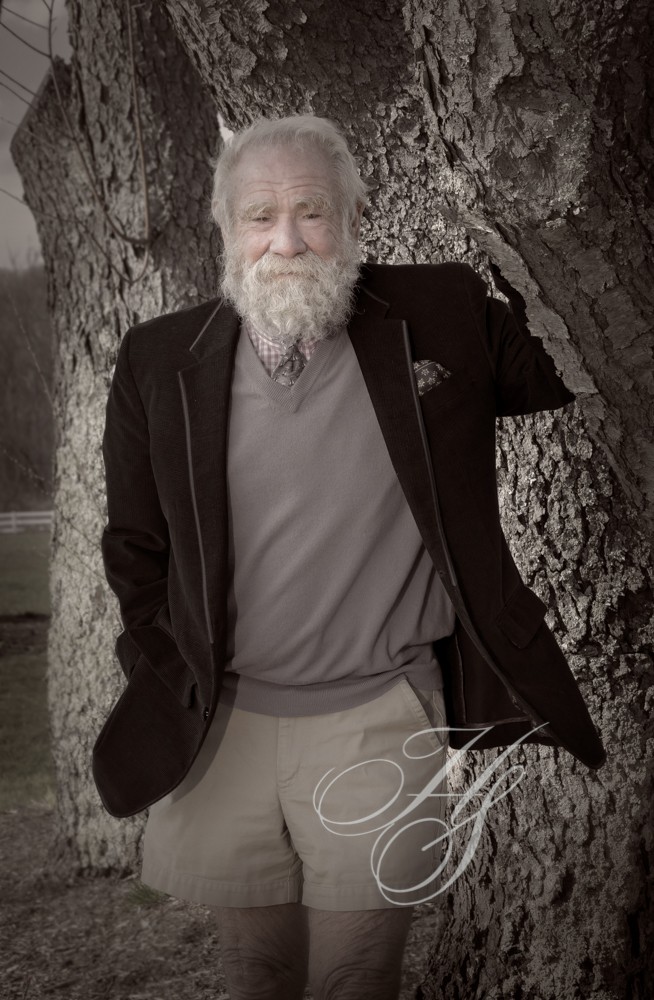 A man with long white beard leaning against a tree.