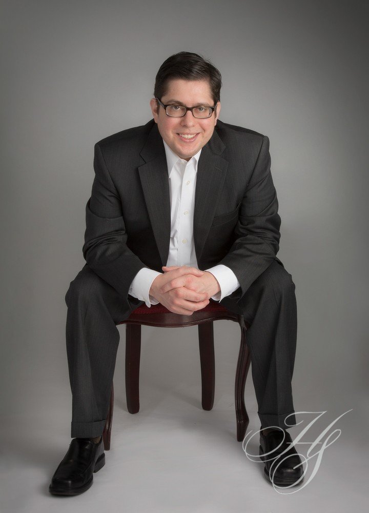 A man in suit and glasses sitting on a chair.