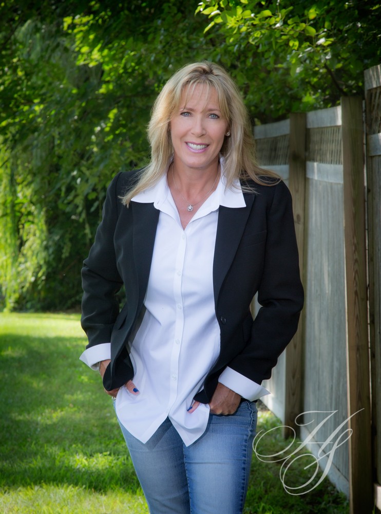 A woman in black jacket and white shirt standing next to fence.