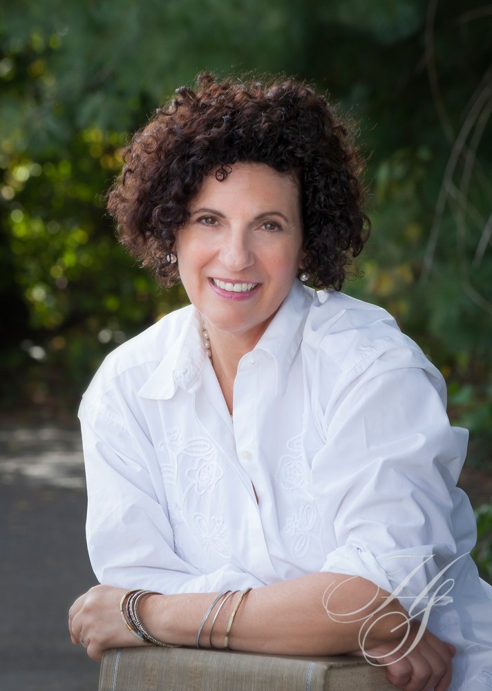 A woman with curly hair sitting outside in front of trees.