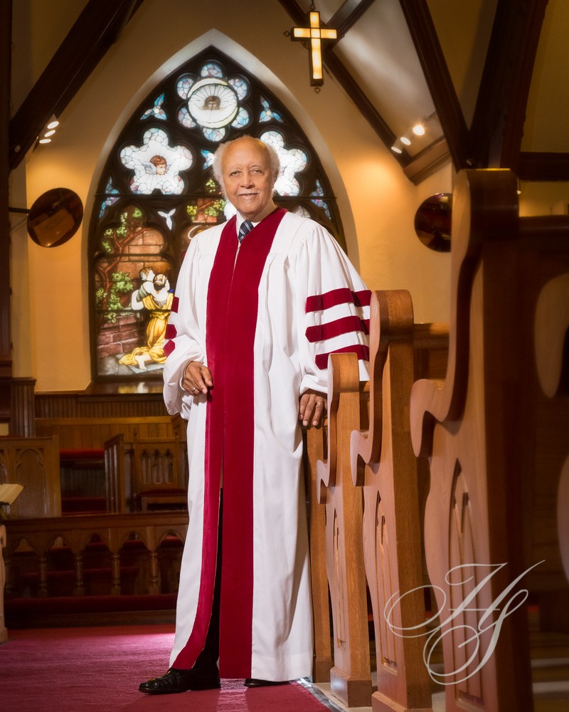 A man in robe standing next to wooden pews.