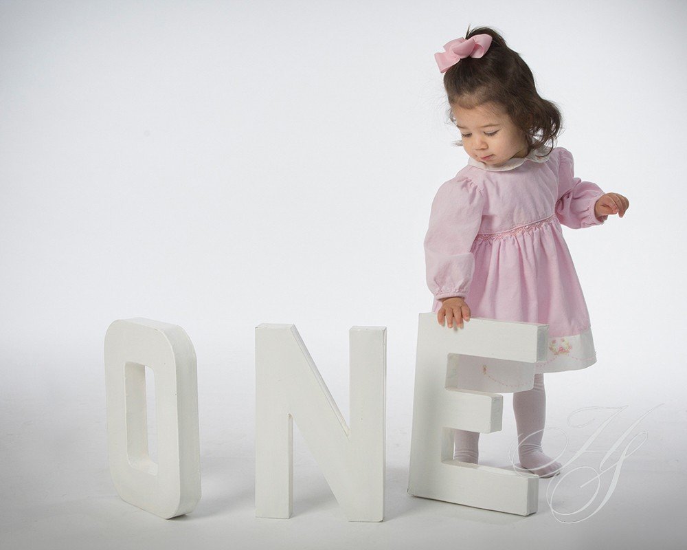 A little girl in pink dress standing next to the word " one ".