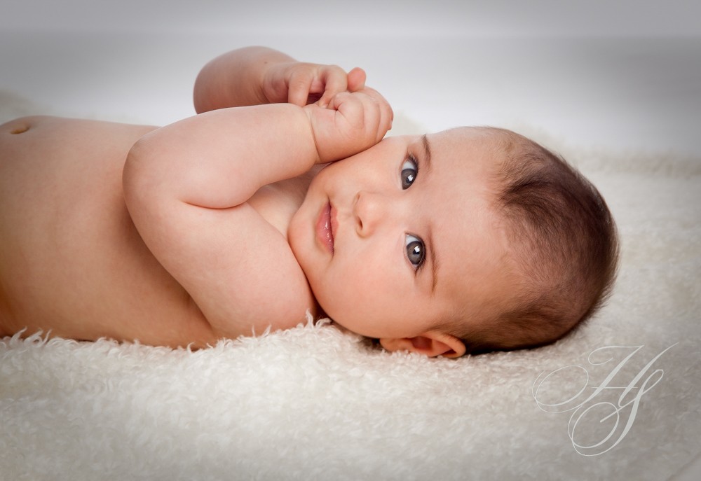 A baby laying on the ground with its hands up.
