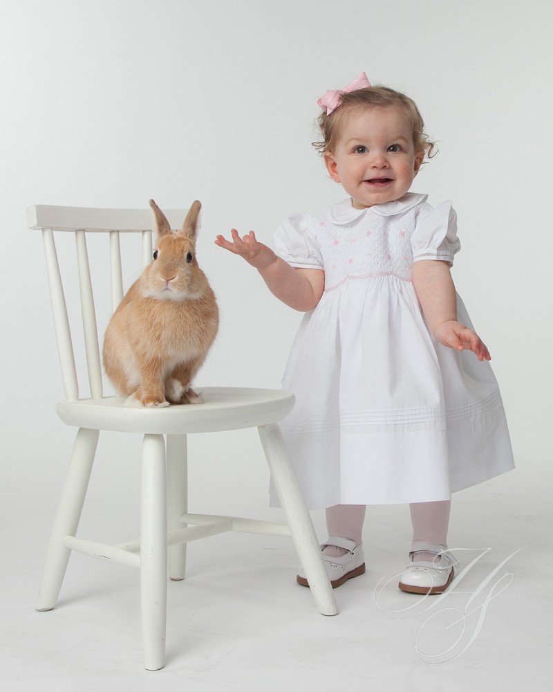 A baby girl standing next to a bunny rabbit.