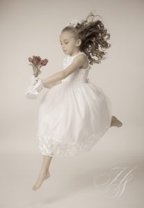 A young girl in white dress holding flowers.