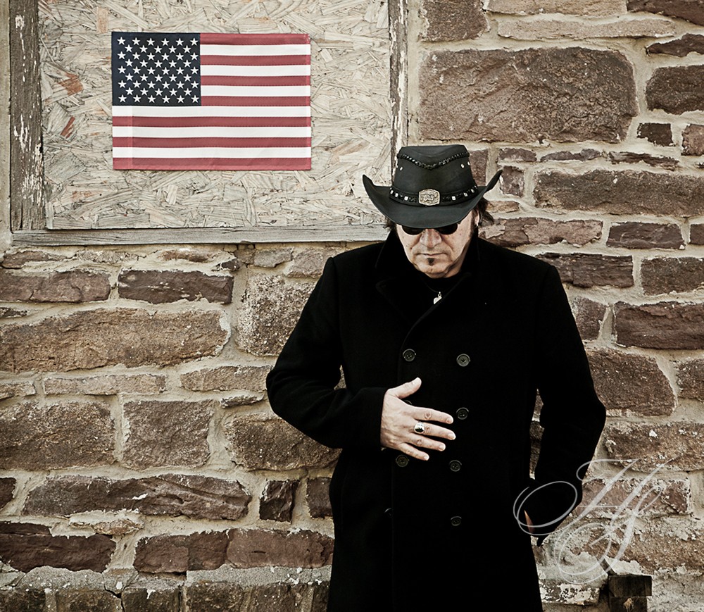 A man in black jacket and hat near brick wall.