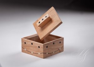 A wooden box with a lid open and a small hole in the top.