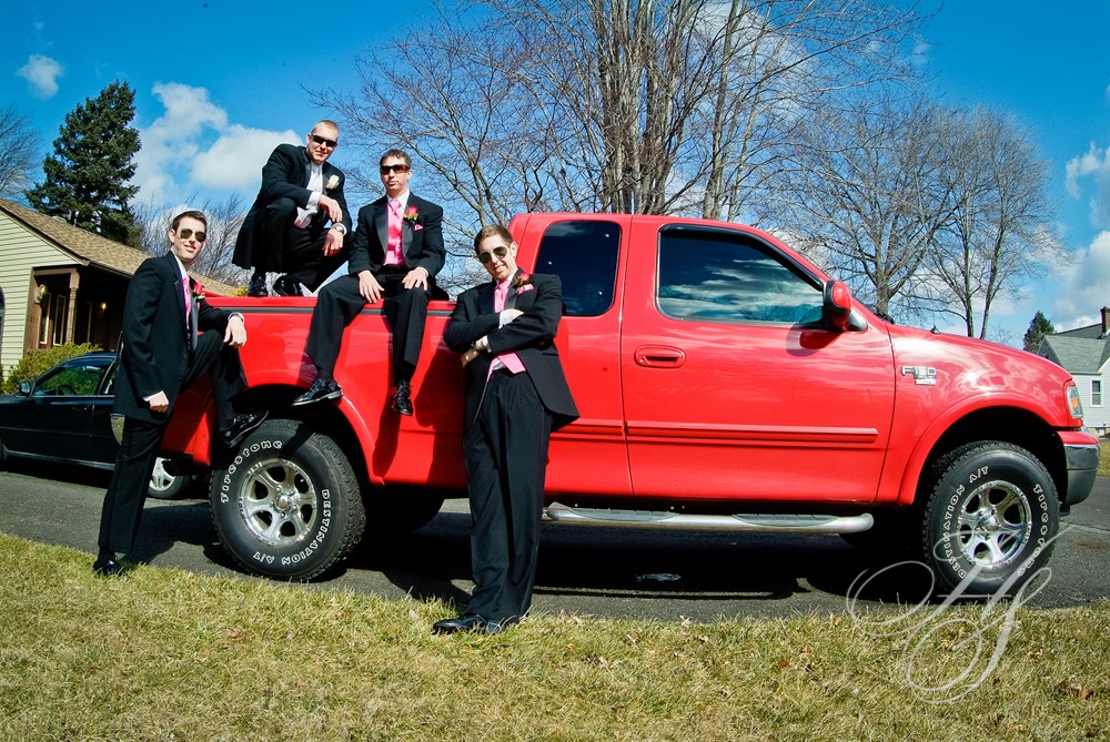 A group of people in suits sitting on the back of a red truck.