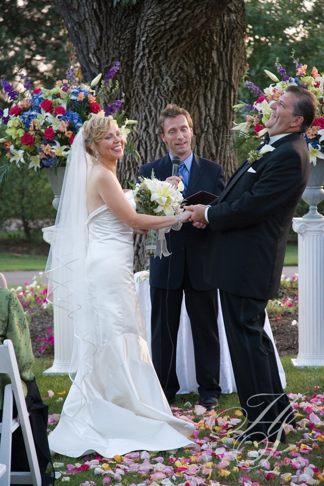 A bride and groom are holding hands while the officiant is holding flowers.