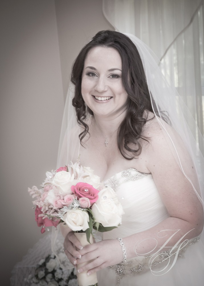 A bride holding her bouquet of flowers in front of the window.