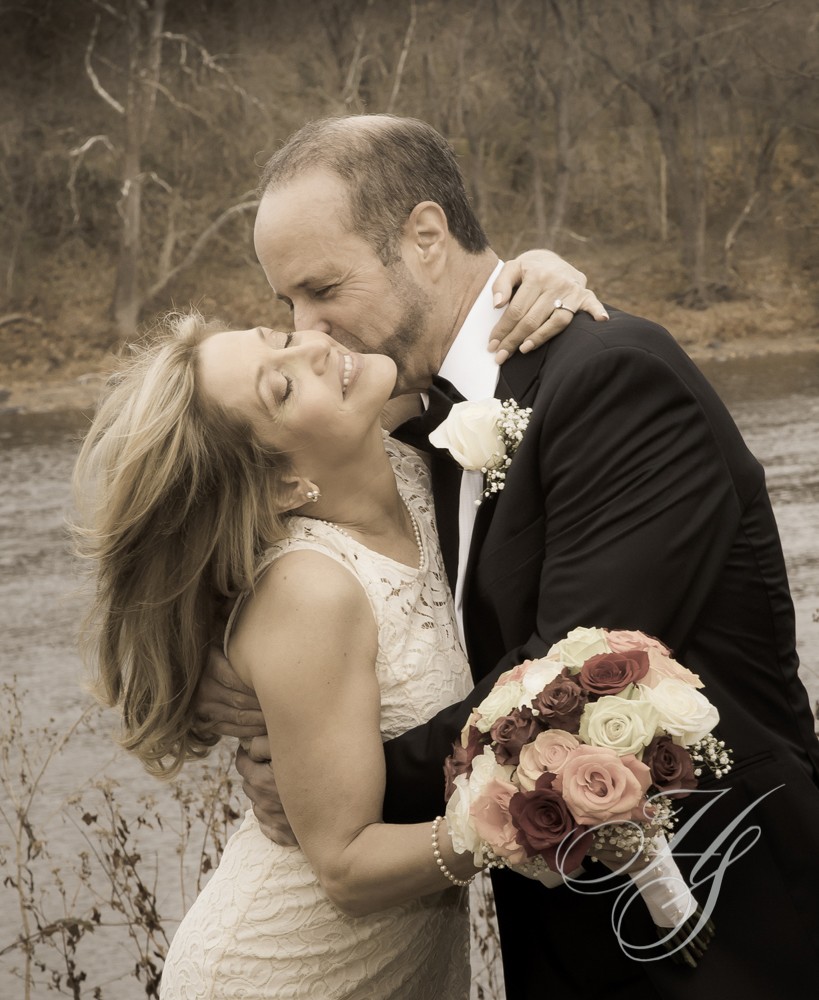 A man and woman kissing in front of trees.