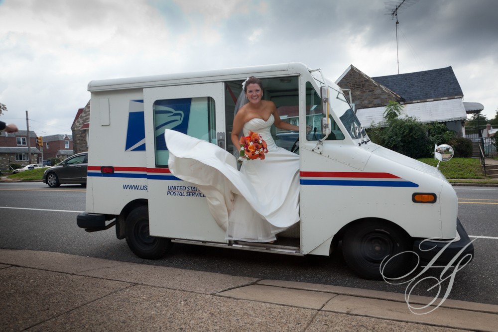 A bride in wedding dress sitting inside of mail truck.