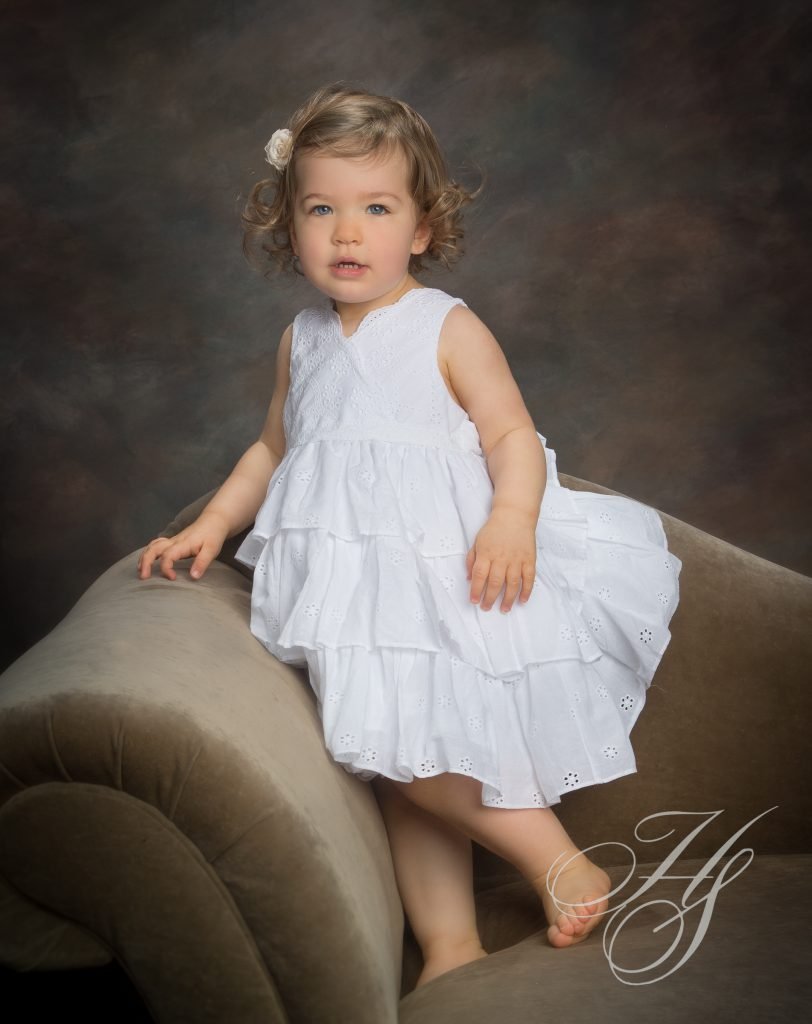 A little girl in white dress sitting on top of a chair.