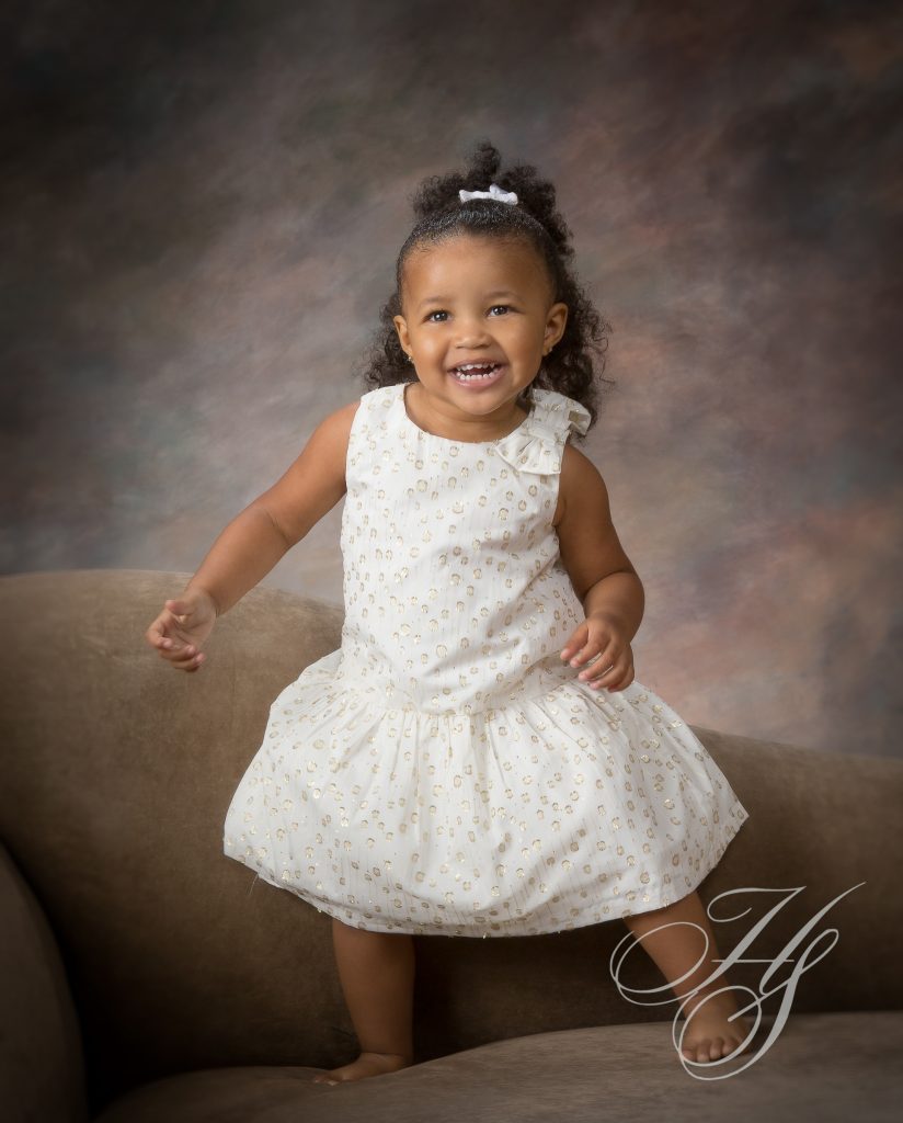 A little girl in white dress on brown couch.
