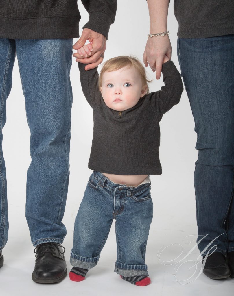 A baby is holding hands with two adults.