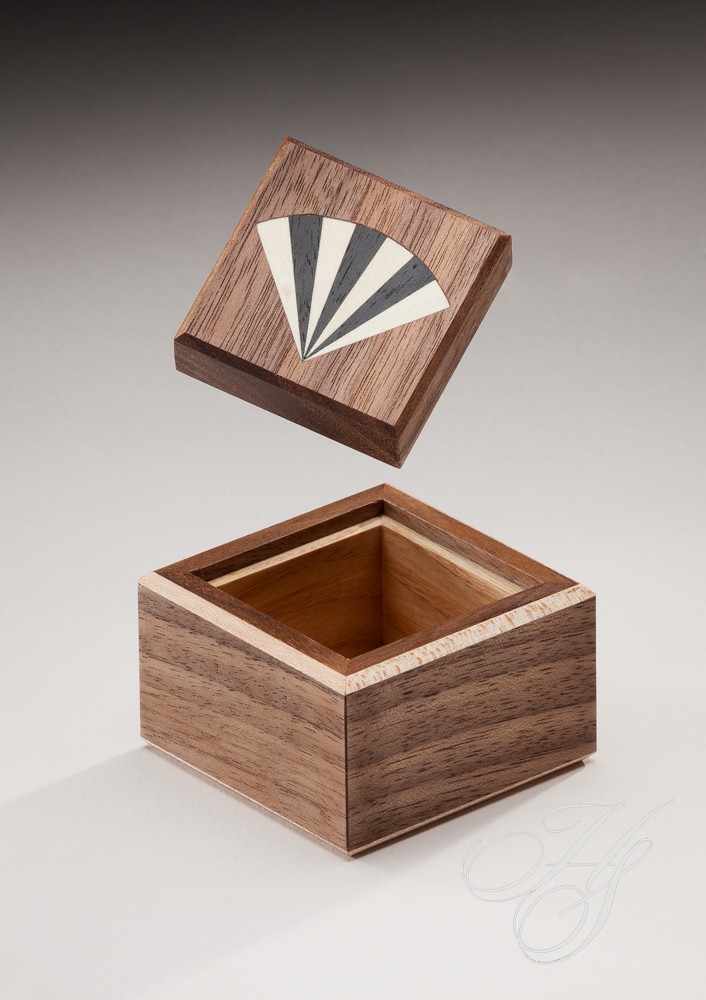 A wooden box with an open lid and a fan design on the top.