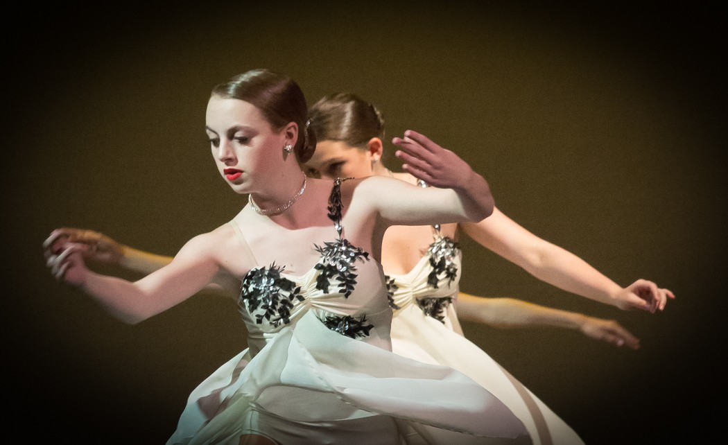 Two women in white dresses are dancing on a stage.