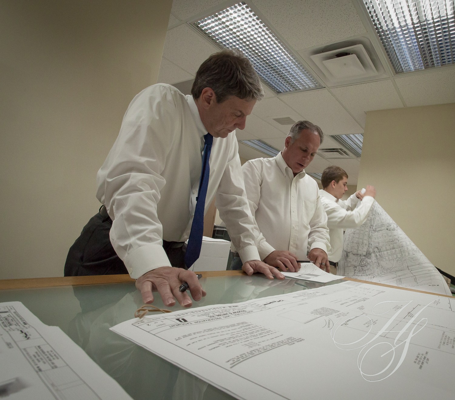 Three men in suits and ties are looking at plans.