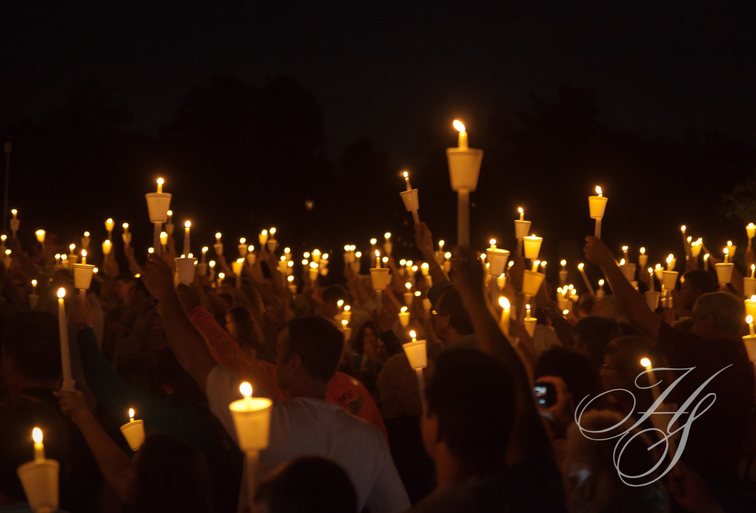 A crowd of people holding lit candles in the dark.