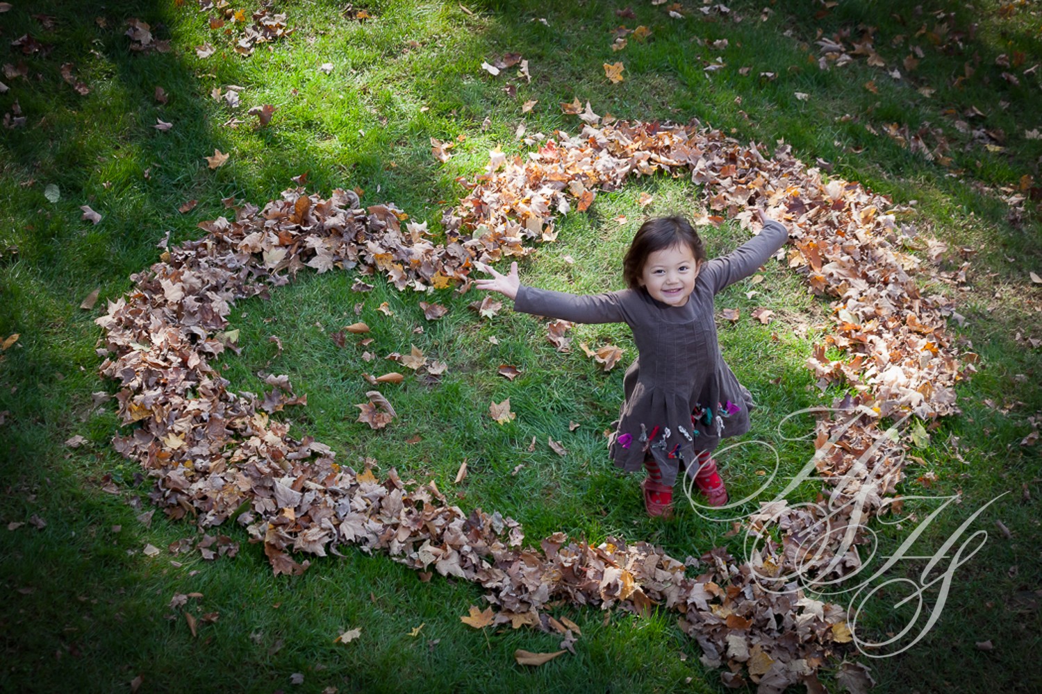 A little girl standing in the grass with leaves around her.