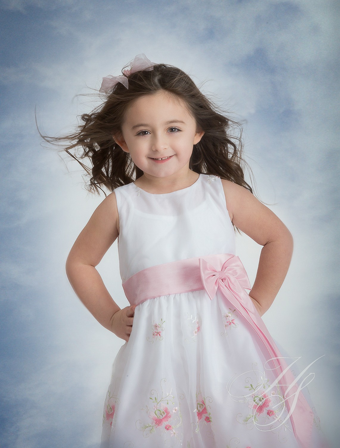 A little girl in white dress with pink ribbon.