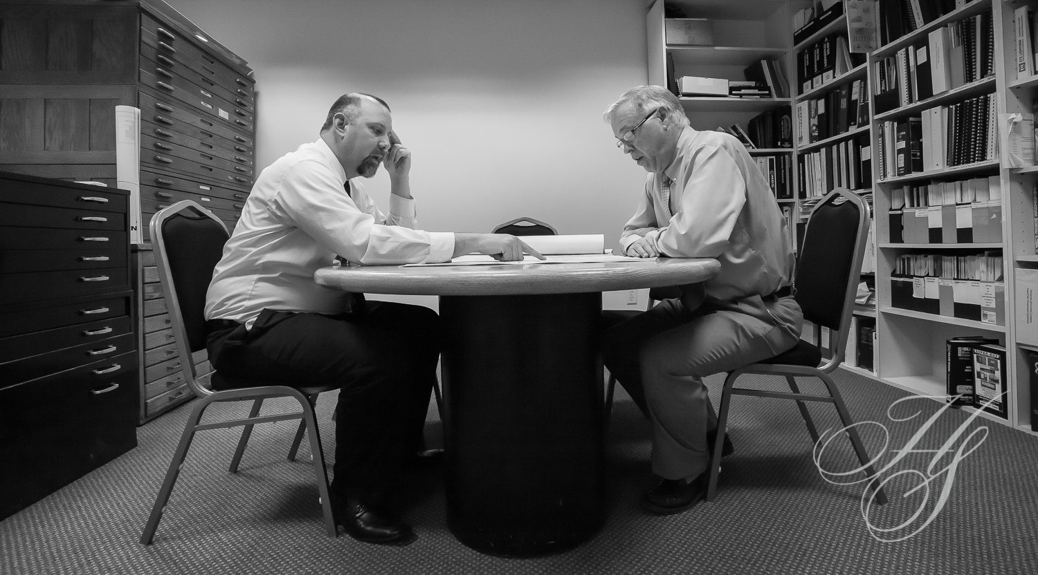 Two men sitting at a table with papers on it.