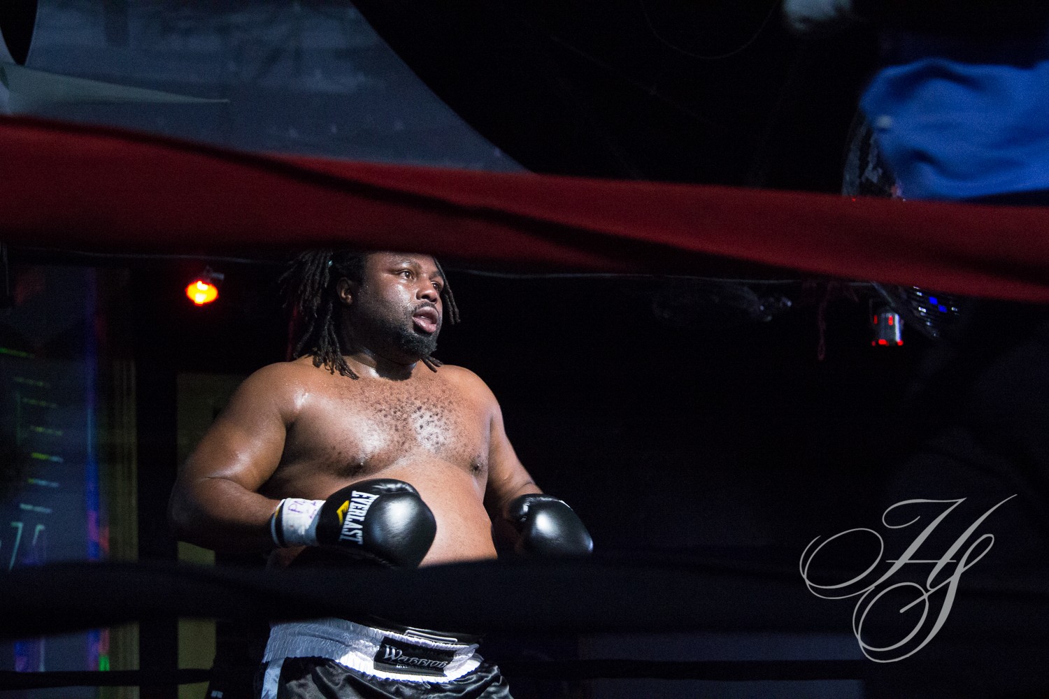 A man in boxing gloves stands on the ropes.
