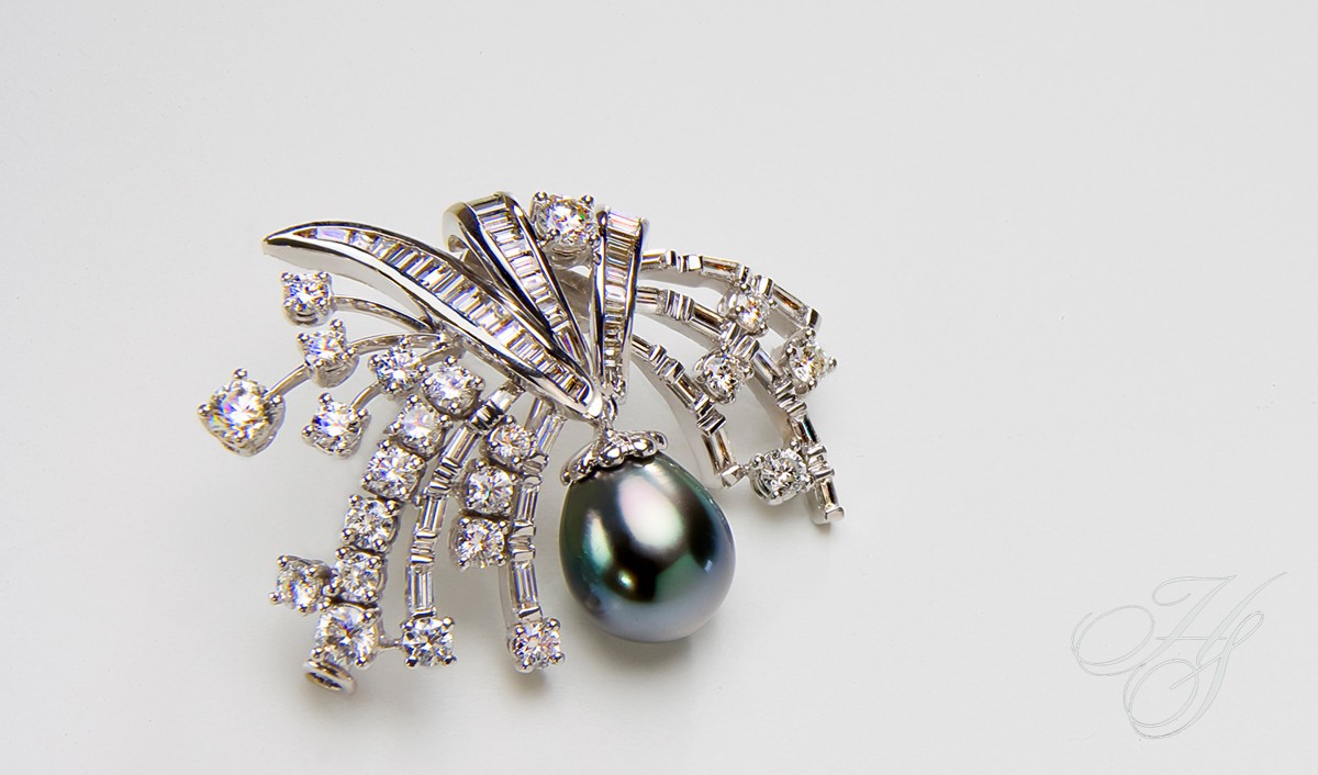 A black pearl is hanging on the side of a diamond brooch.