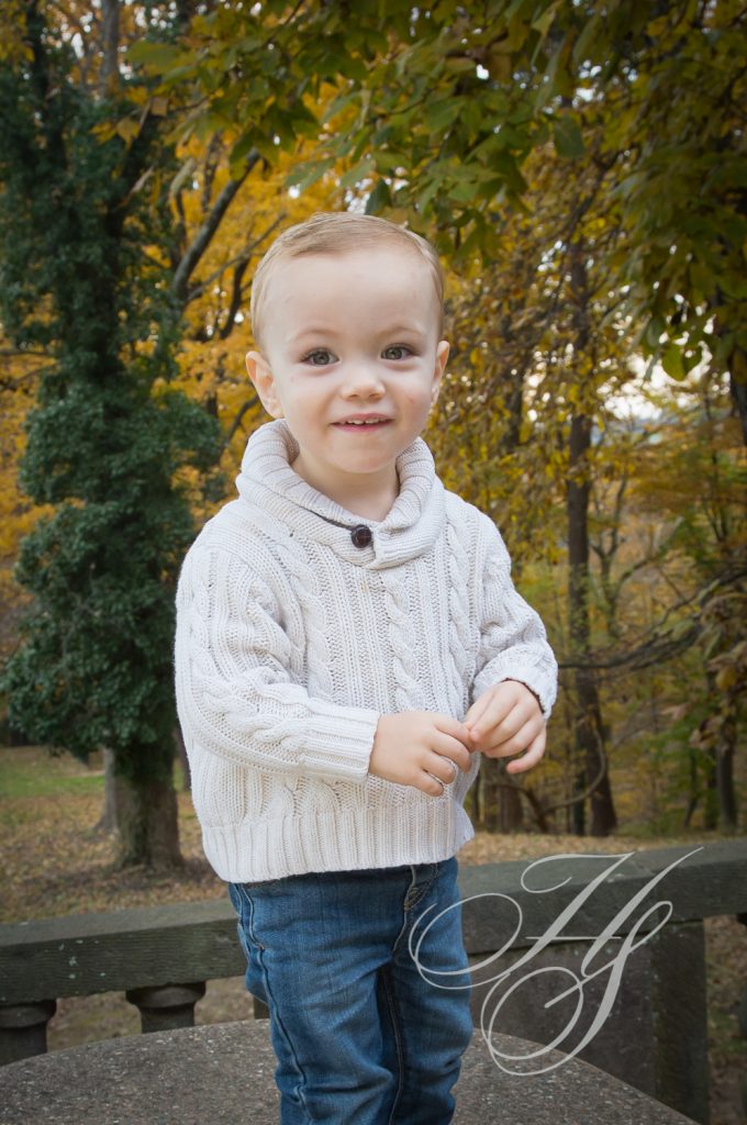 A young boy in white sweater near trees.