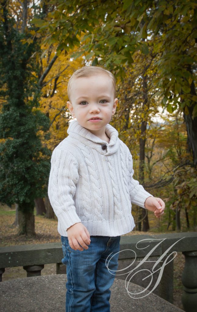A young boy in white sweater standing next to trees.
