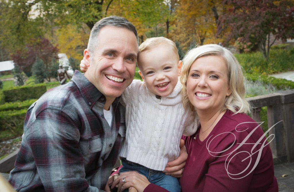 A man and woman holding a child in front of trees.