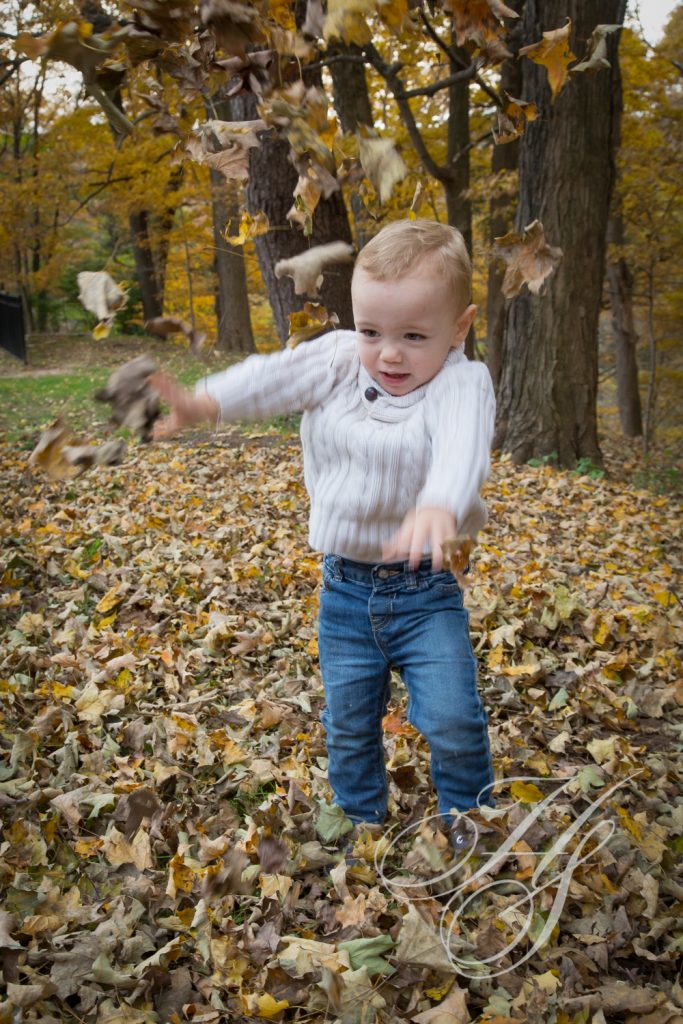 A toddler is playing in the leaves outside.