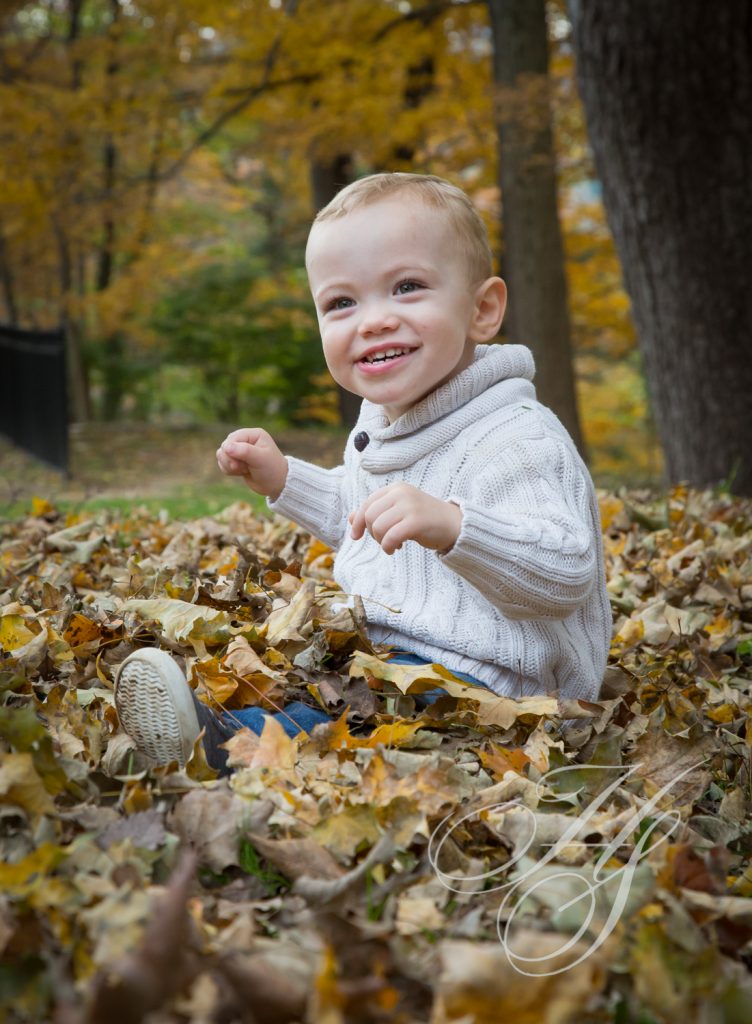 A baby sitting in the leaves on the ground