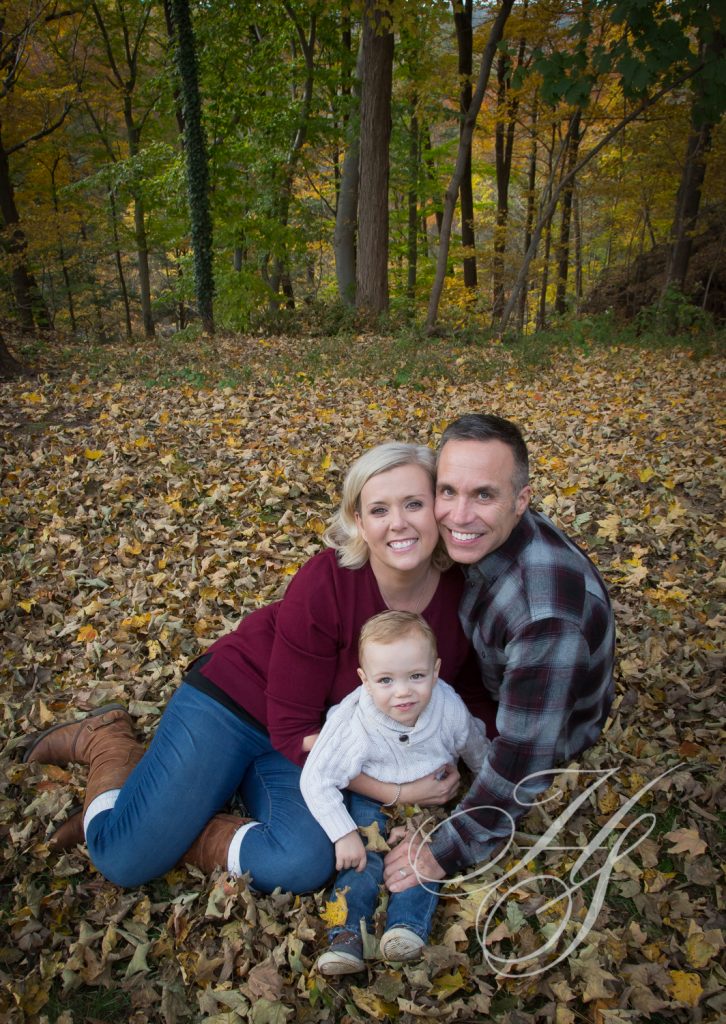 A man, woman and baby sitting in the leaves.