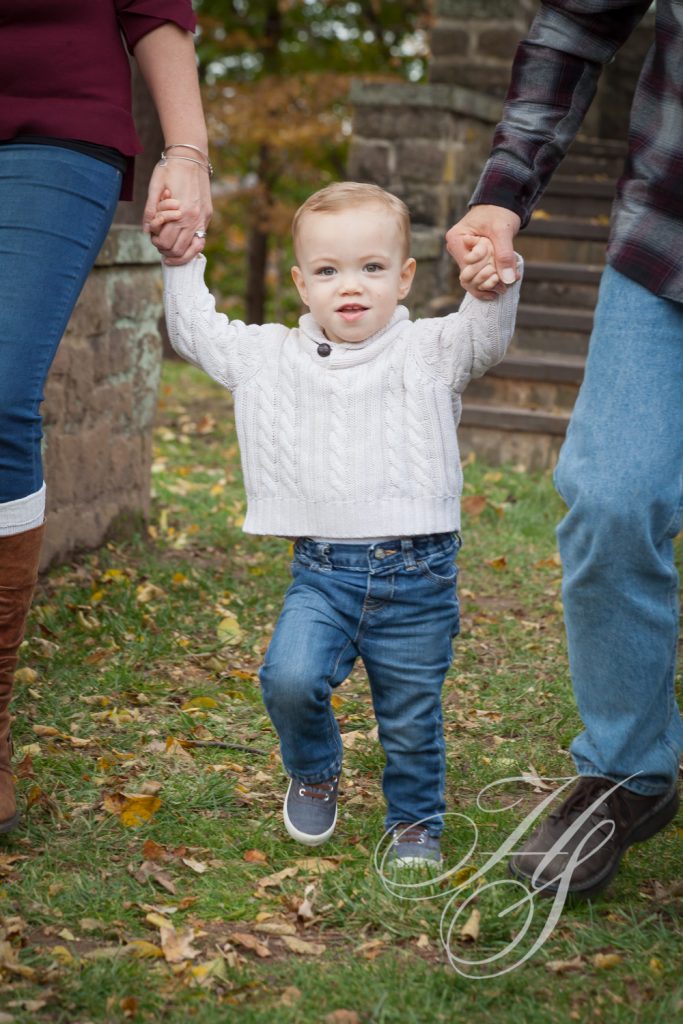 A little boy holding his hands with two adults.