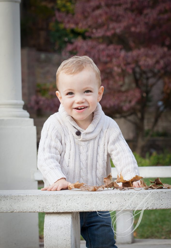 A young boy is smiling while playing with leaves.