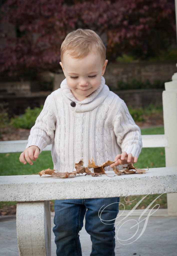 A toddler is playing with leaves on the ground.