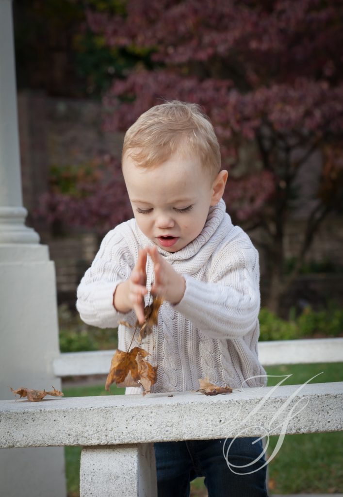 A baby is playing with leaves outside.