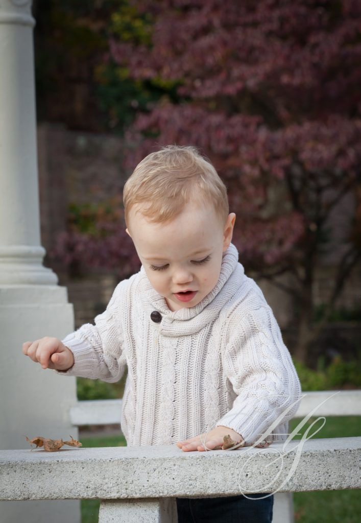 A baby in white sweater standing on top of a fence.