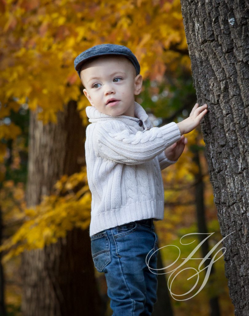 A young boy in a hat leaning against a tree.