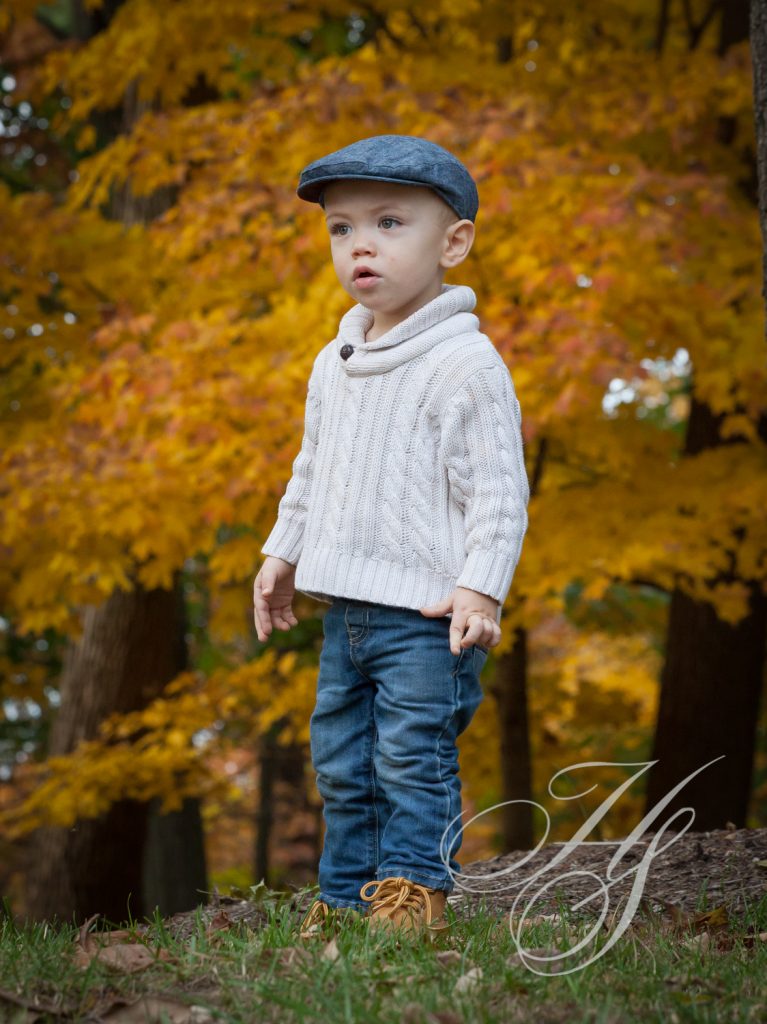 A young boy in a hat and sweater stands on the ground.