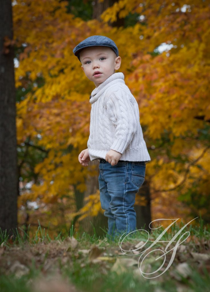 A young boy in white shirt and hat standing on grass.