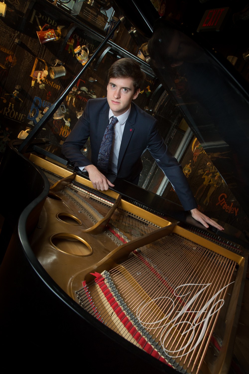 A man in suit and tie standing next to an open piano.