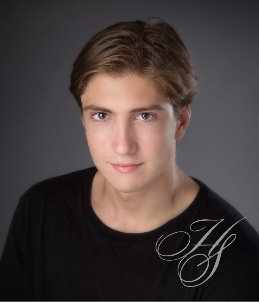 A young man posing for a photo in front of a gray background.