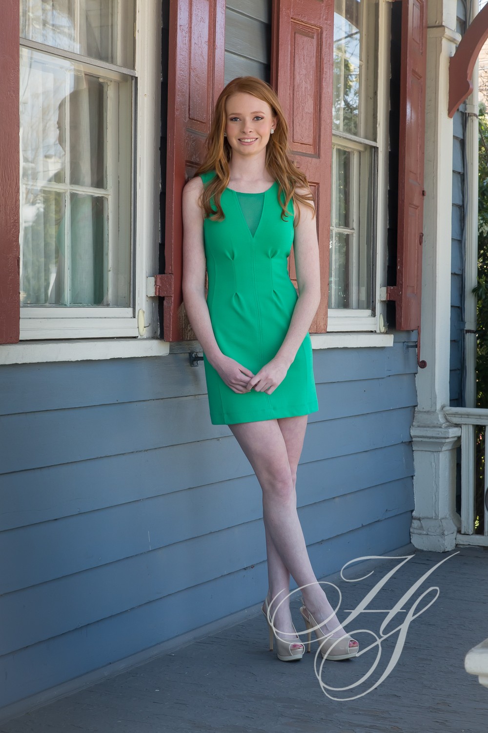 A girl in a green dress standing on the porch.