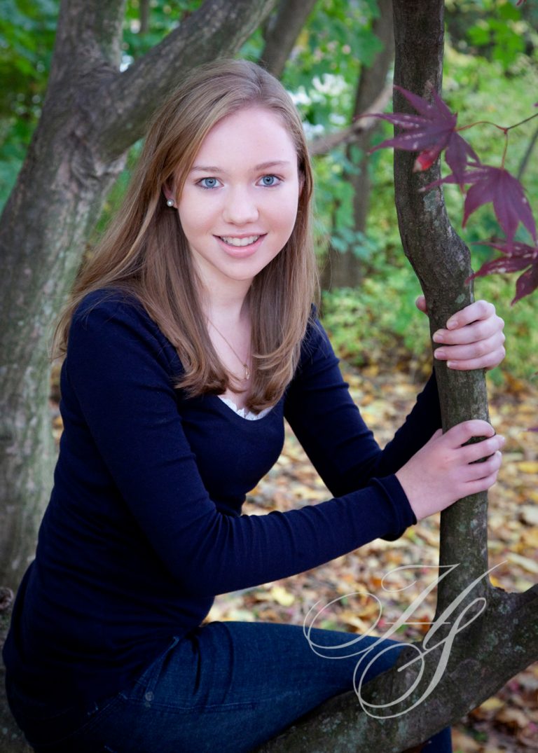 A girl leaning on a tree branch in the woods.