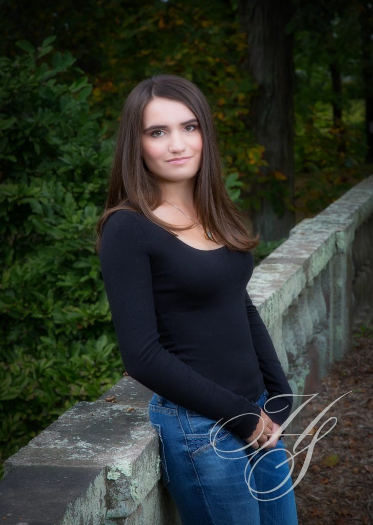 A beautiful young lady standing next to a stone wall.