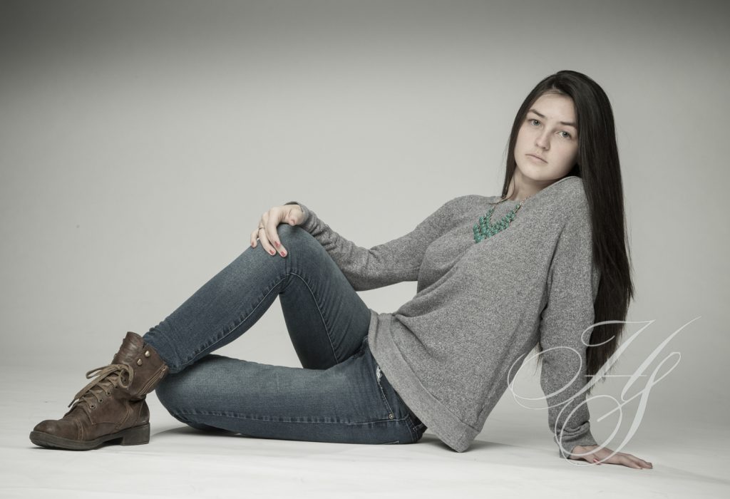 A woman sitting on the ground wearing jeans and boots.
