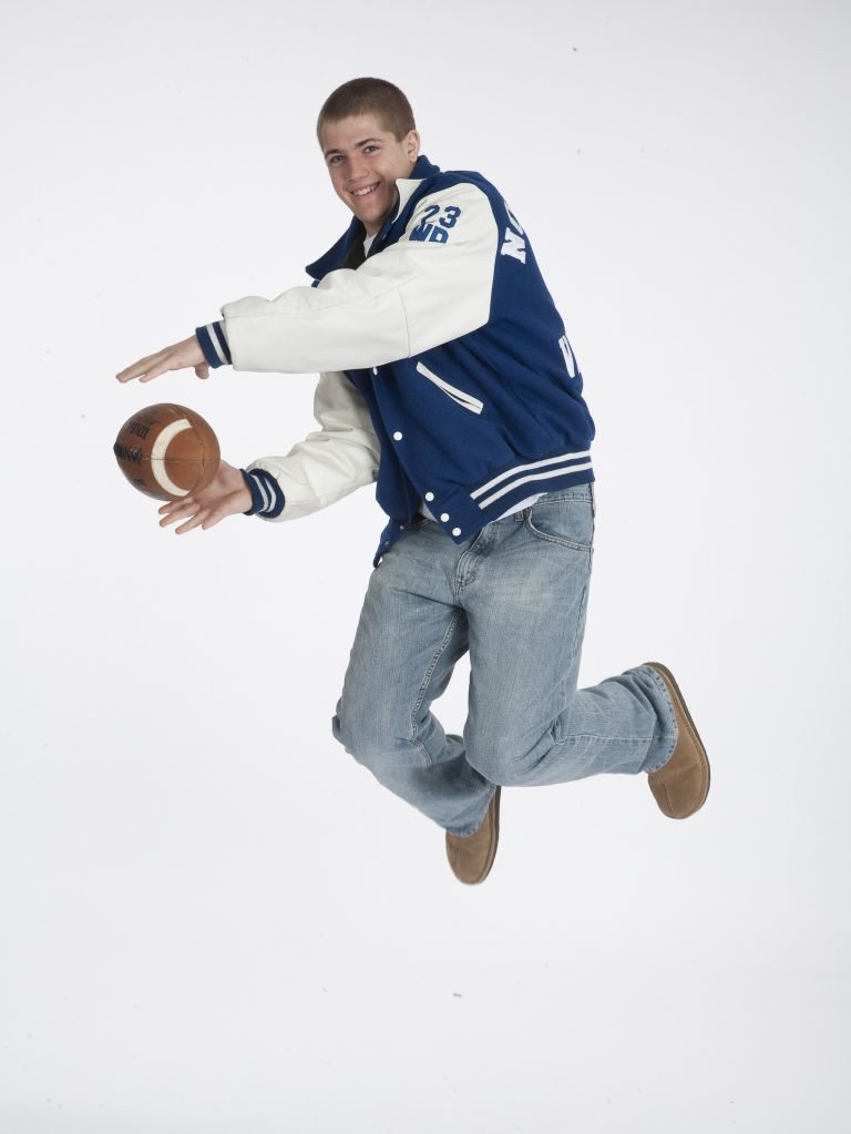 A man in blue jacket jumping with football.